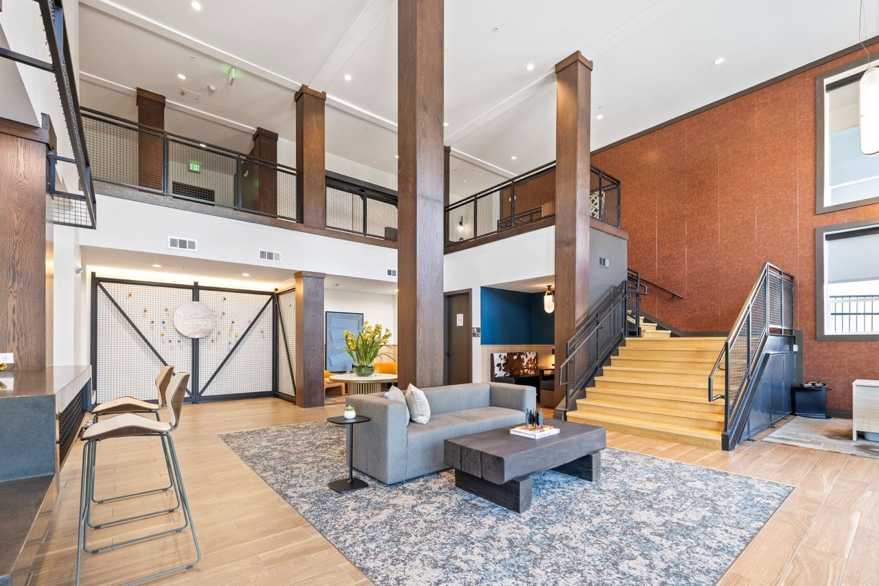 Open lobby with a gray sofa, coffee table, tall wooden columns, and a staircase to the upper level.