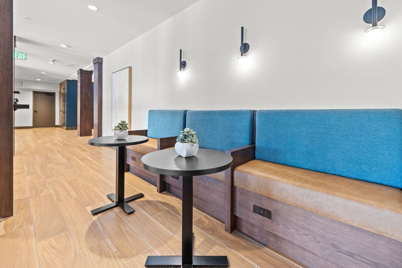 The Lock at Flatirons Lobby seating area in a modern apartment community with blue upholstered benches and round black tables.