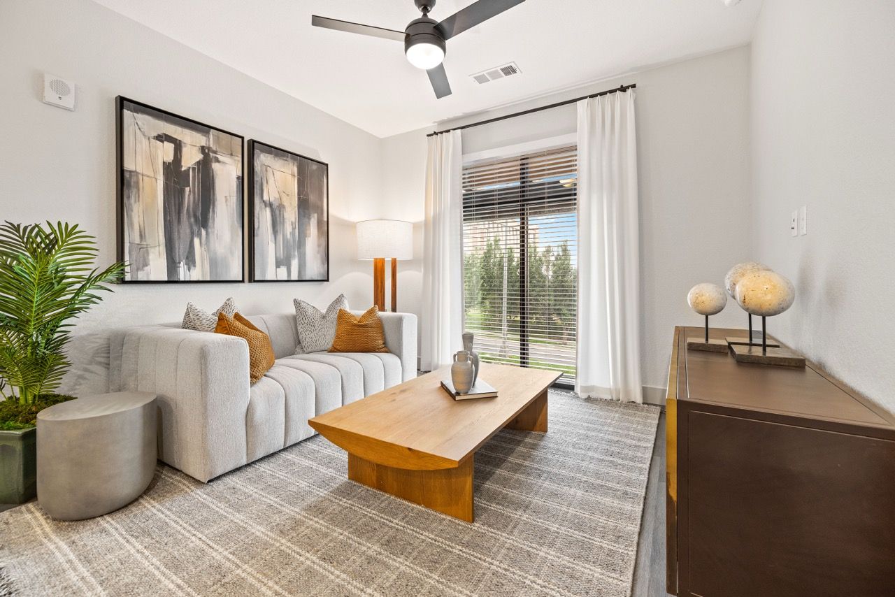 The Lock at Flatirons Living room with gray sofa, wooden coffee table, rug, and a large window with blinds.
