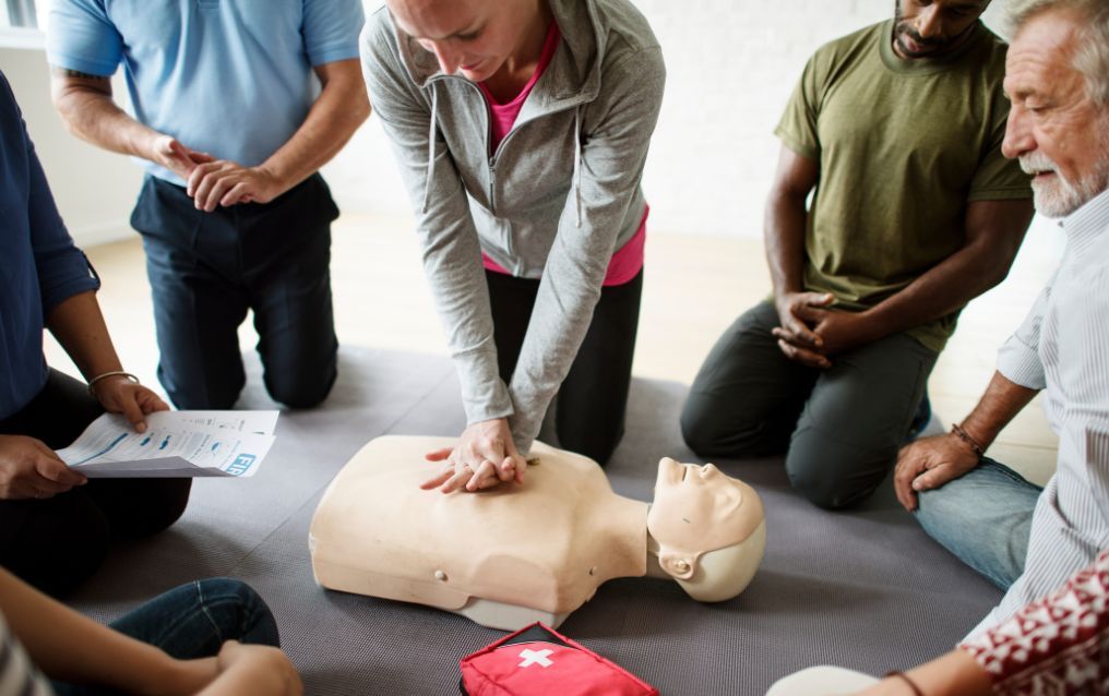 A group of people are sitting around a mannequin.