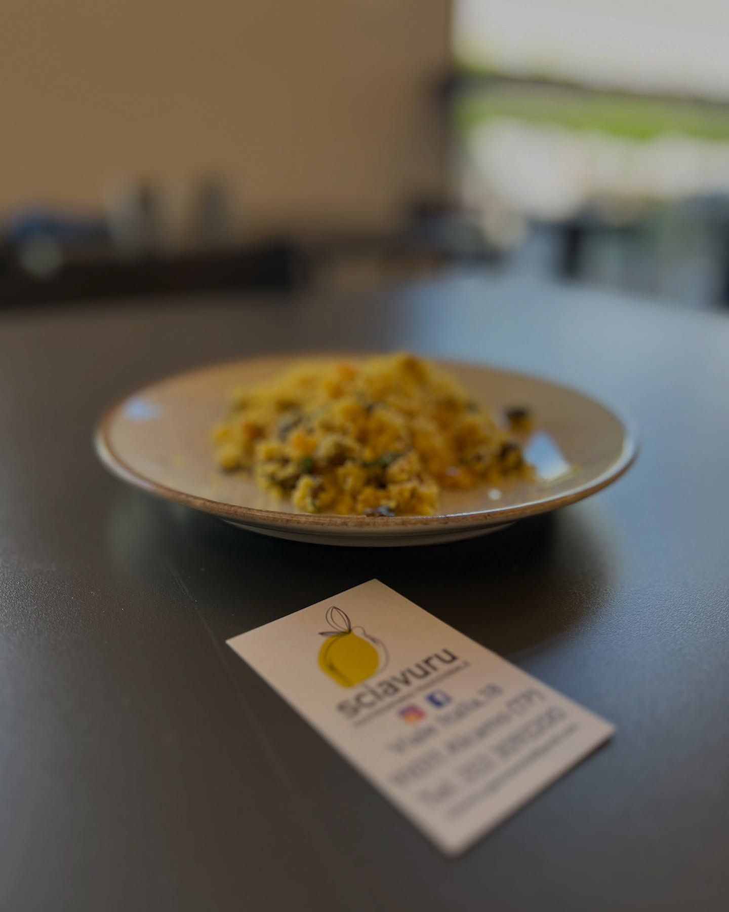 Un piatto di cibo giallo, forse couscous, con un biglietto da visita in primo piano.