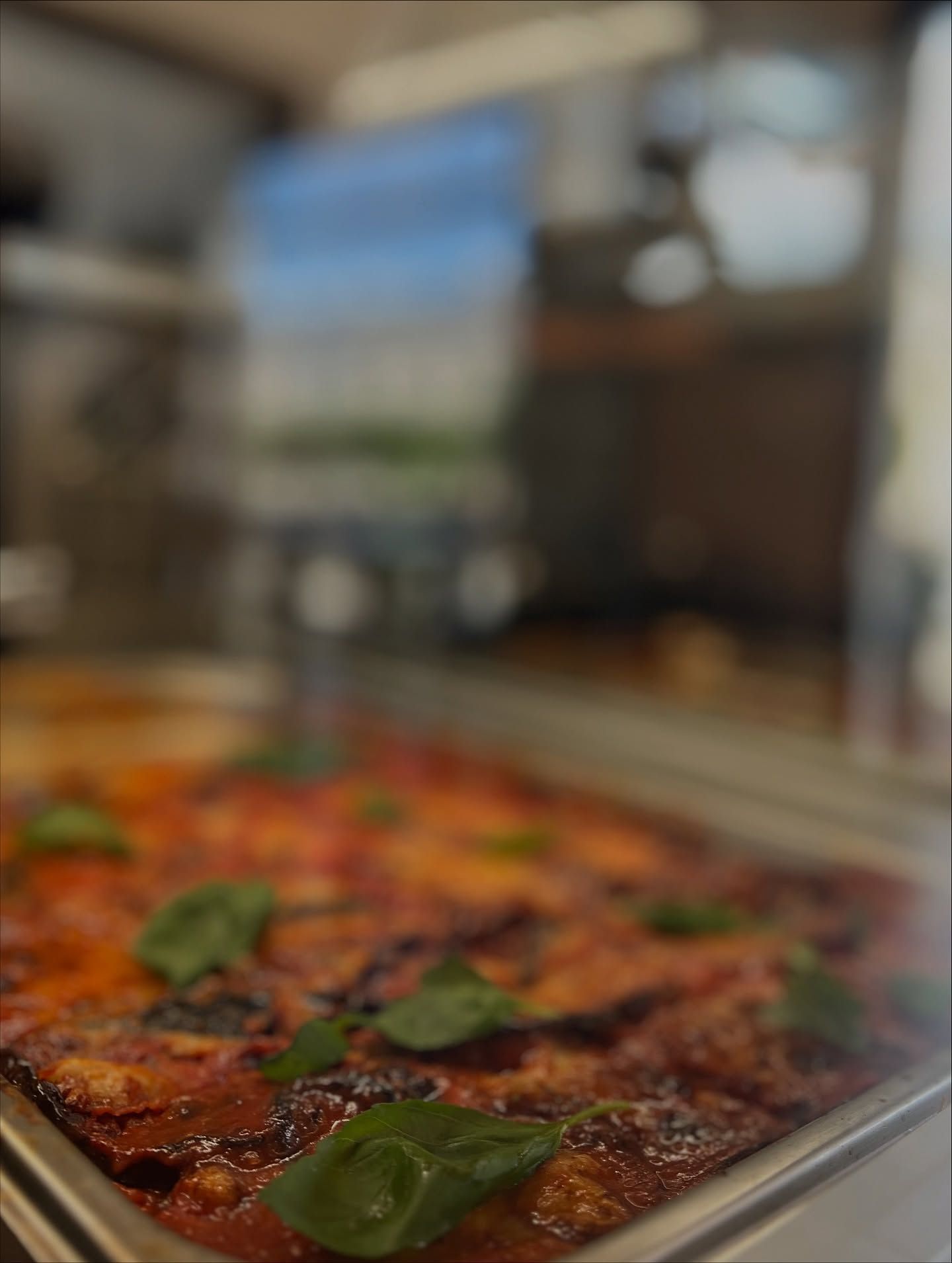 Vassoio di lasagne guarnito con foglie di basilico, in un ambiente da ristorante.