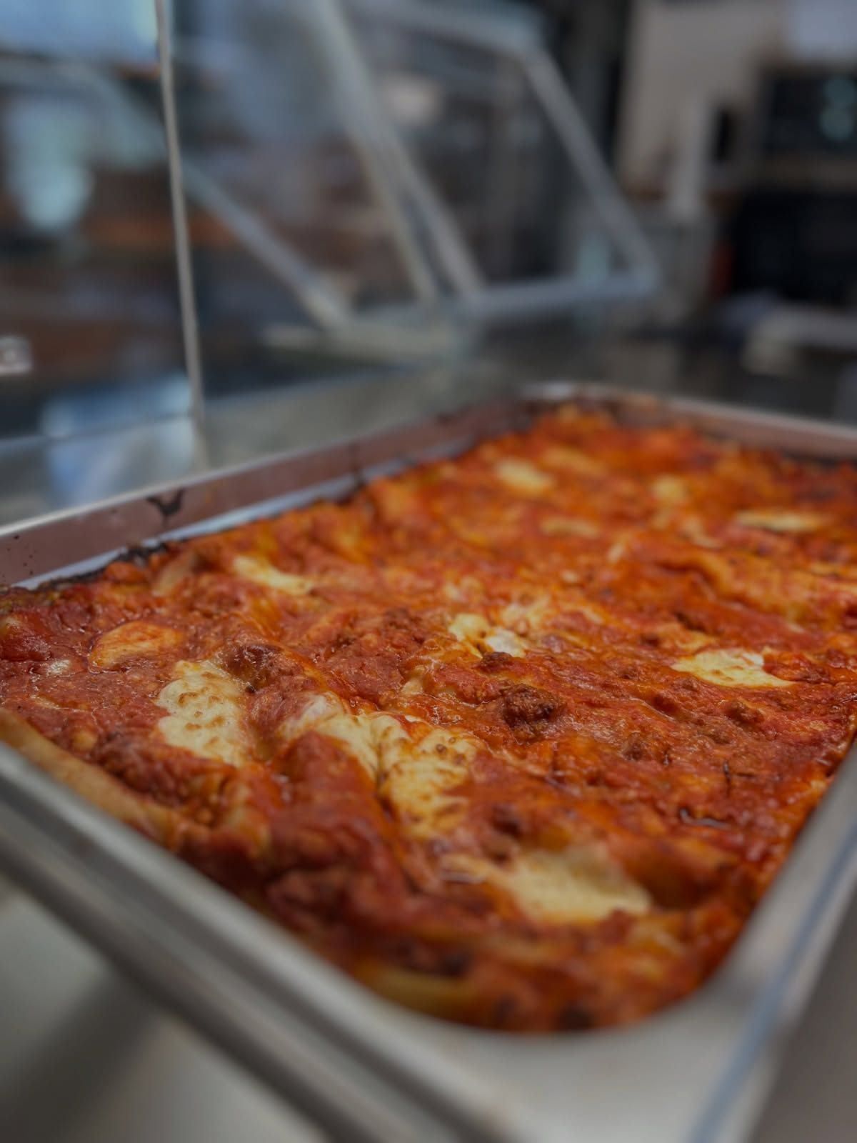 Lasagna in una teglia di metallo, ricoperta di salsa rossa e formaggio fuso.