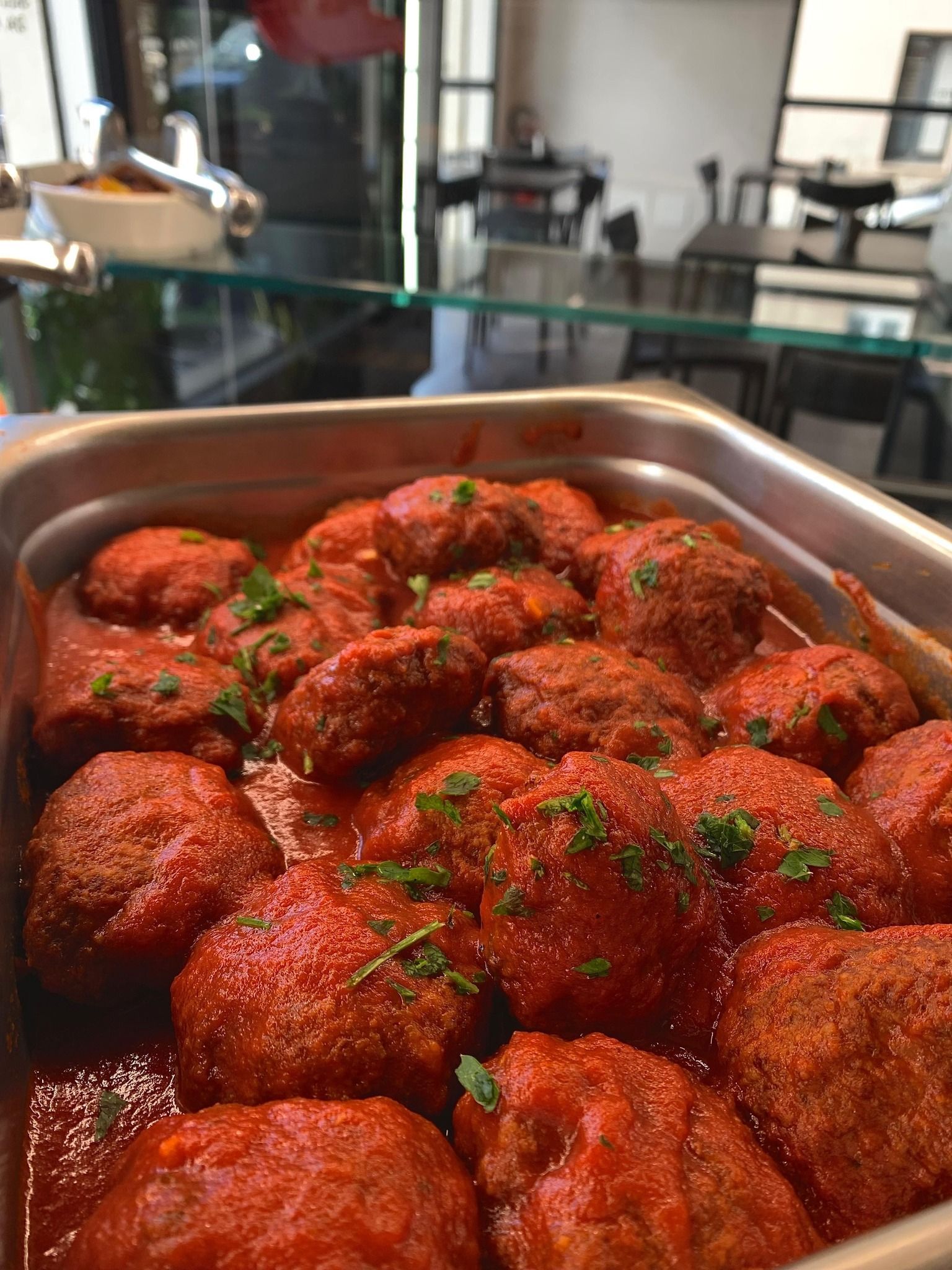 Polpette in salsa rossa, in un vassoio di metallo, guarnite con erbe verdi.