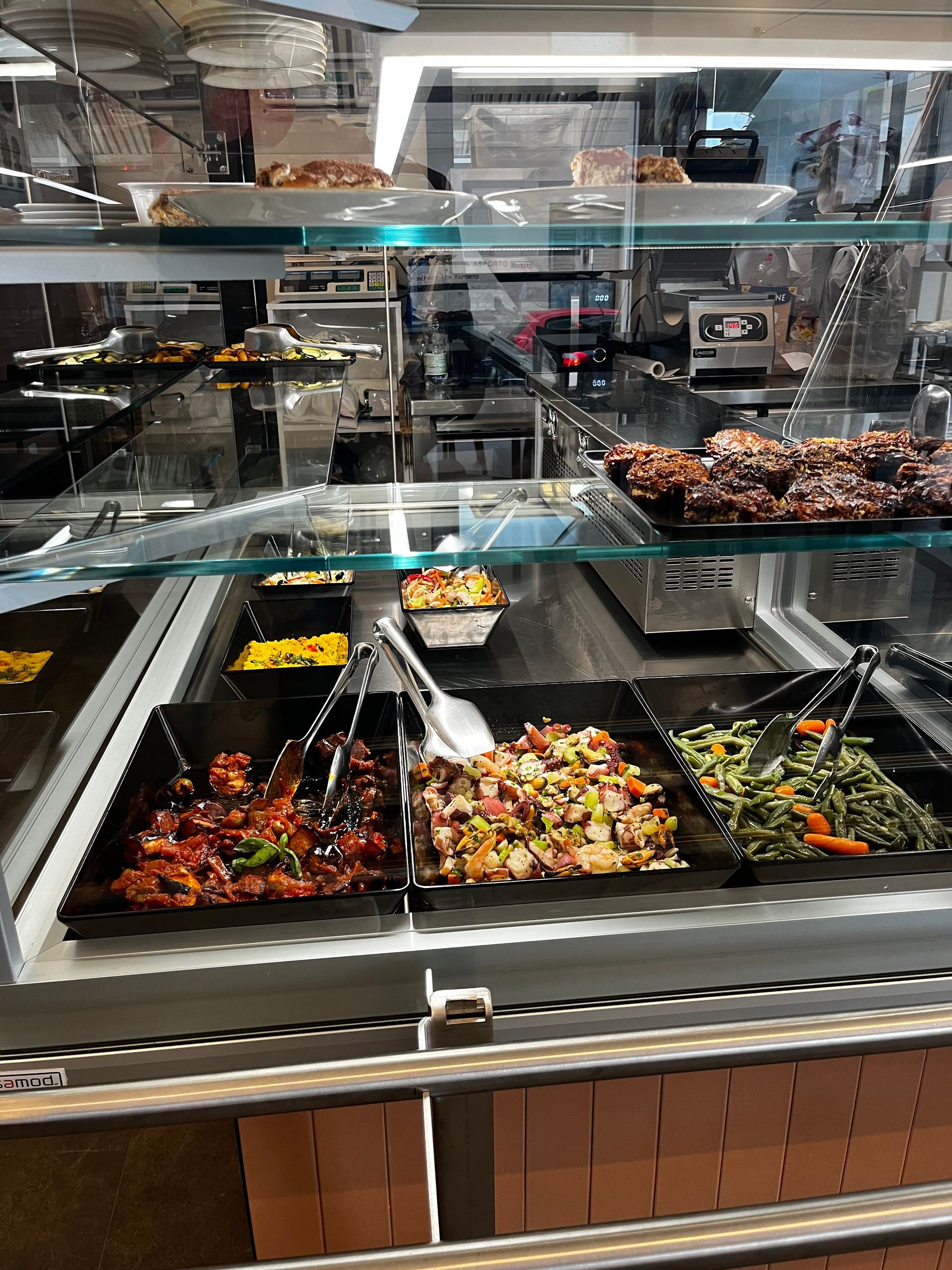 Vetrina espositiva con vari piatti, tra cui insalate e verdure cotte.
