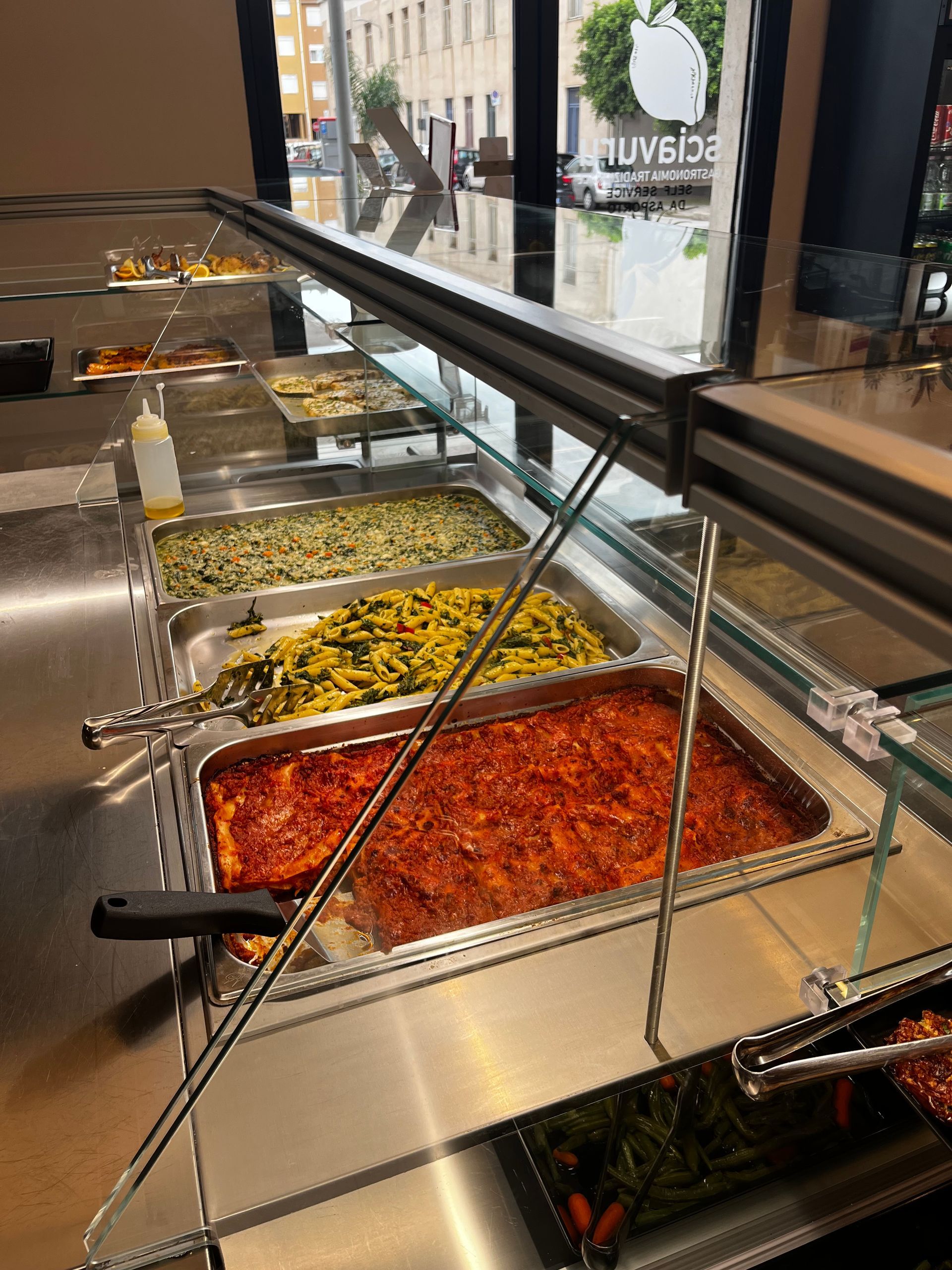 Buffet di cibo con diverse pietanze in contenitori di acciaio inossidabile.