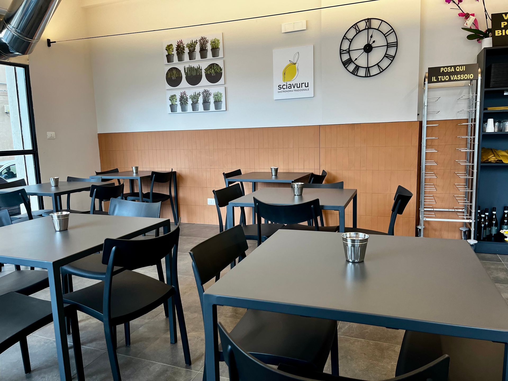 Interno del ristorante con tavoli, sedie e decorazioni murali, tra cui un orologio e poster.