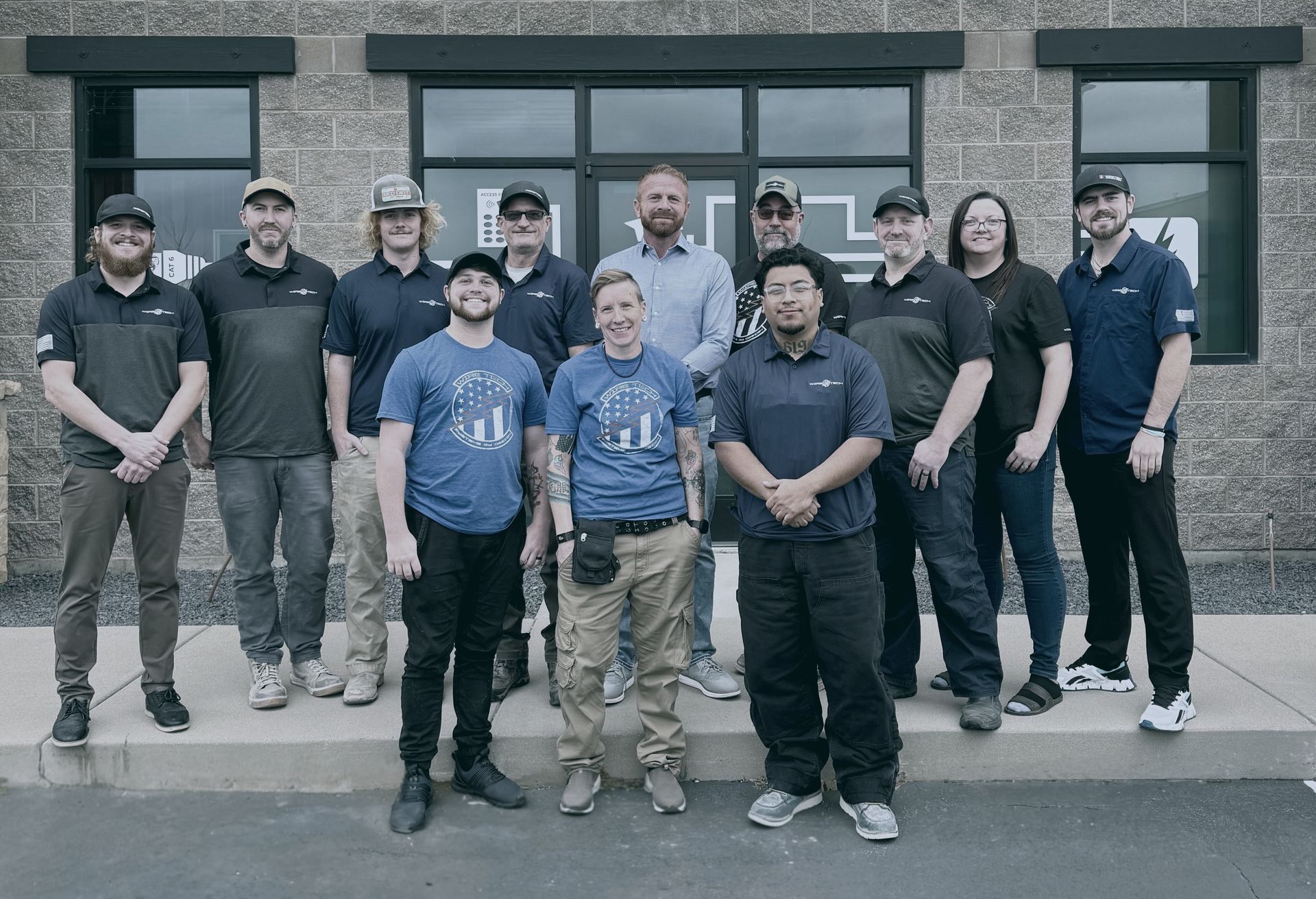 Group of people in front of a building; most wearing dark polo shirts and hats.
