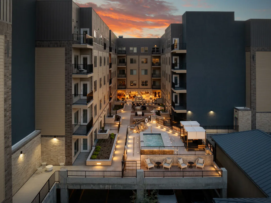Courtyard with pool, seating, and lighting, surrounded by multi-story apartment buildings at sunset.