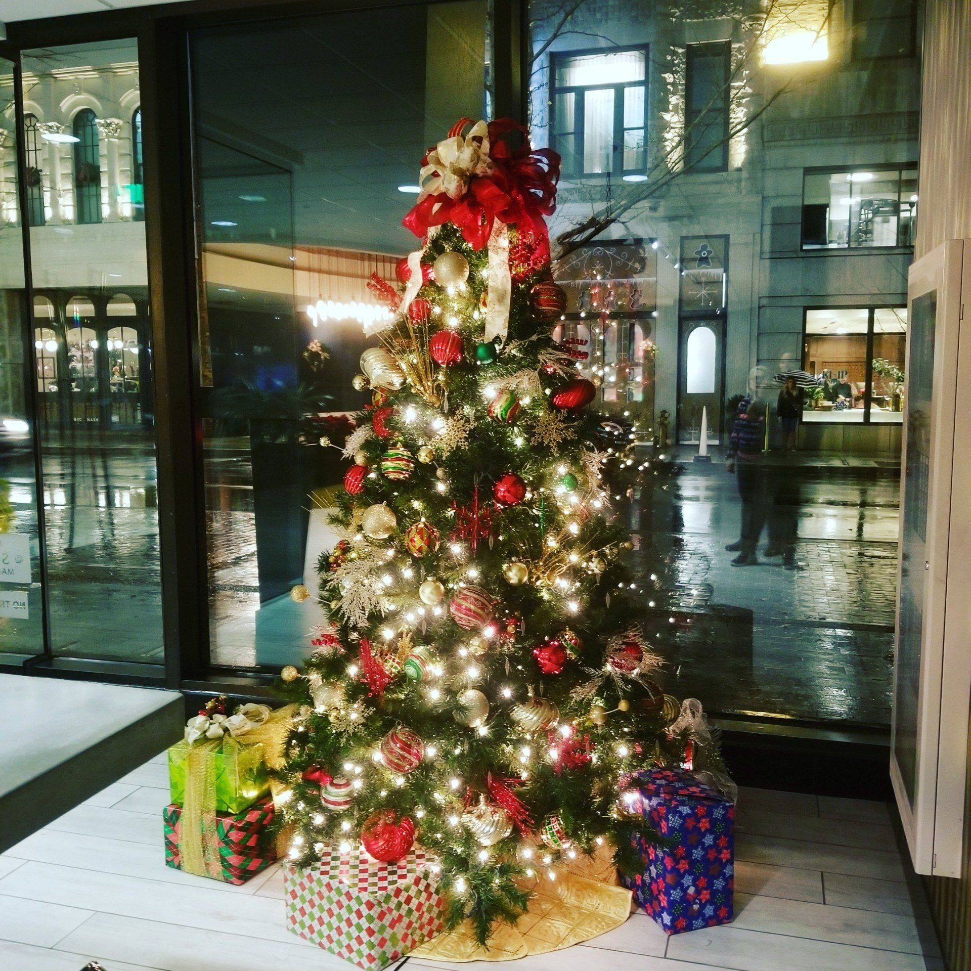 a christmas tree with presents underneath it in front of a window