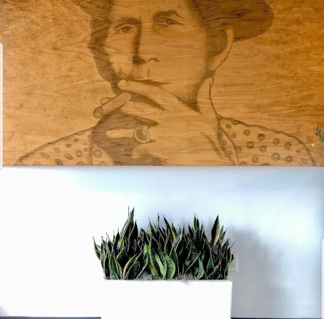 a painting of a woman is hanging on a wall next to a potted plant