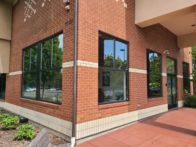 Corner of a brick building with large black-framed windows, reflecting trees and sky.
