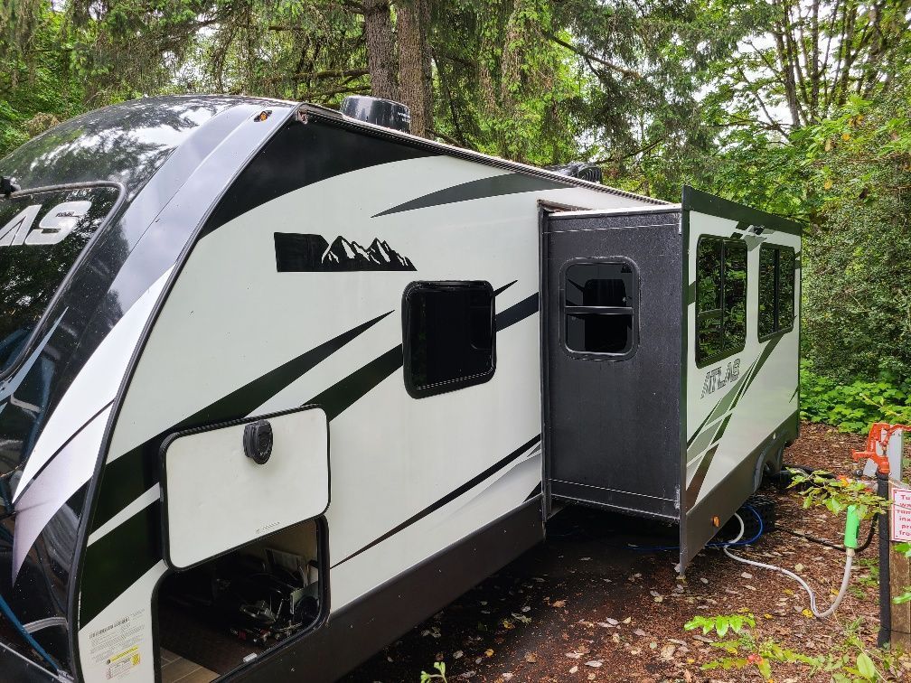 White and black travel trailer with an open door in a wooded campsite.