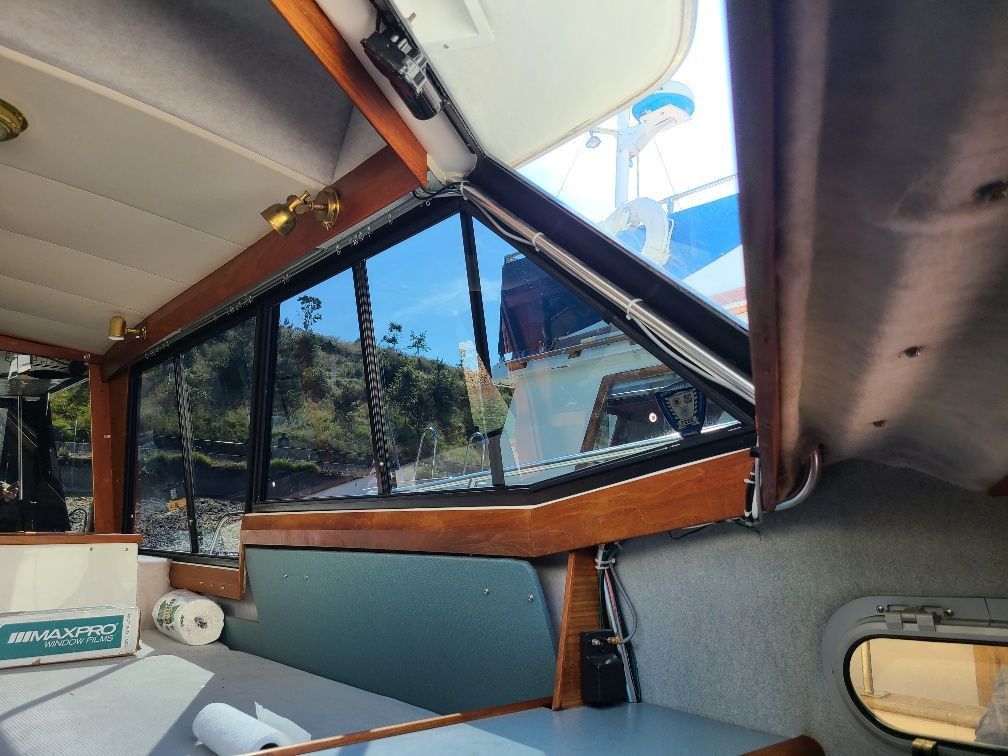 Interior view of a boat cabin with dark windows, wood trim, and glimpses of the outdoors.