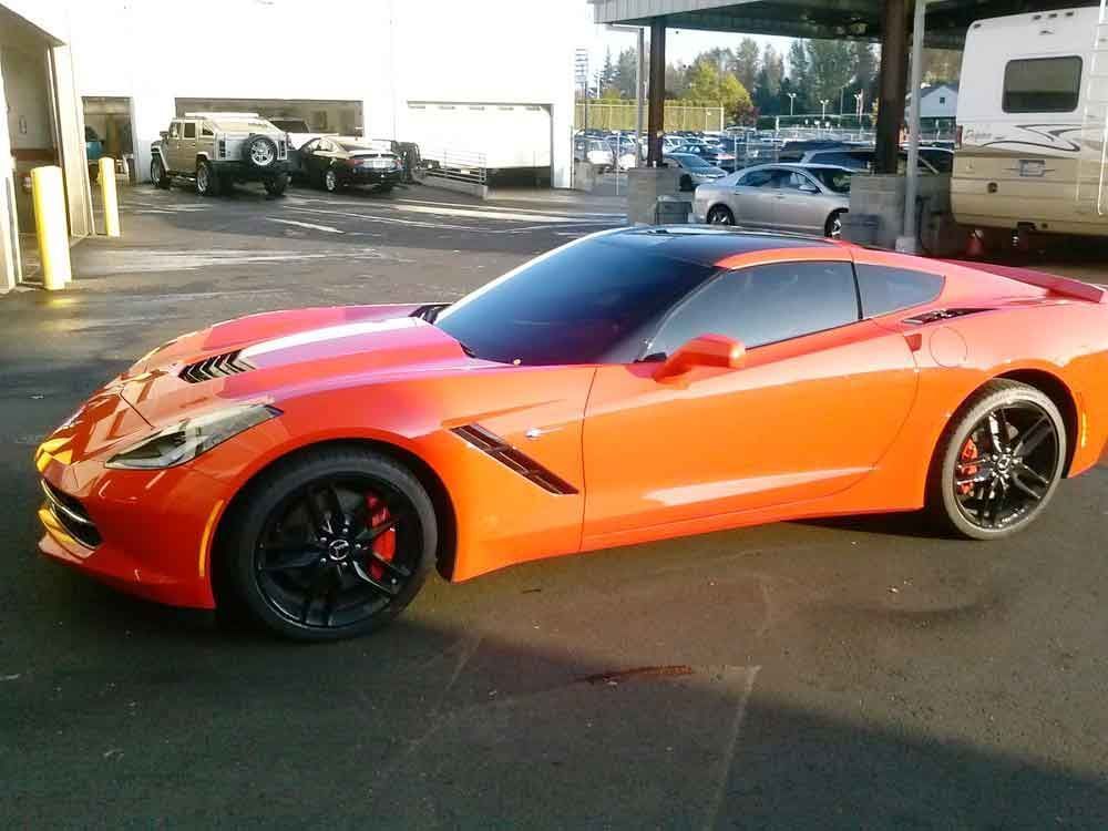 Bright orange Corvette sports car with black rims parked outside a shop.