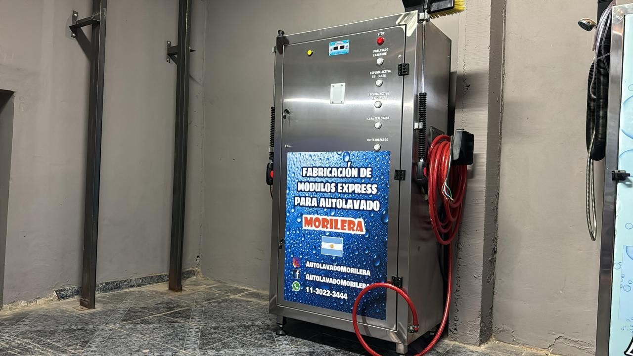 Equipo de lavado de autos de acero inoxidable en un edificio de concreto. Manguera roja conectada.