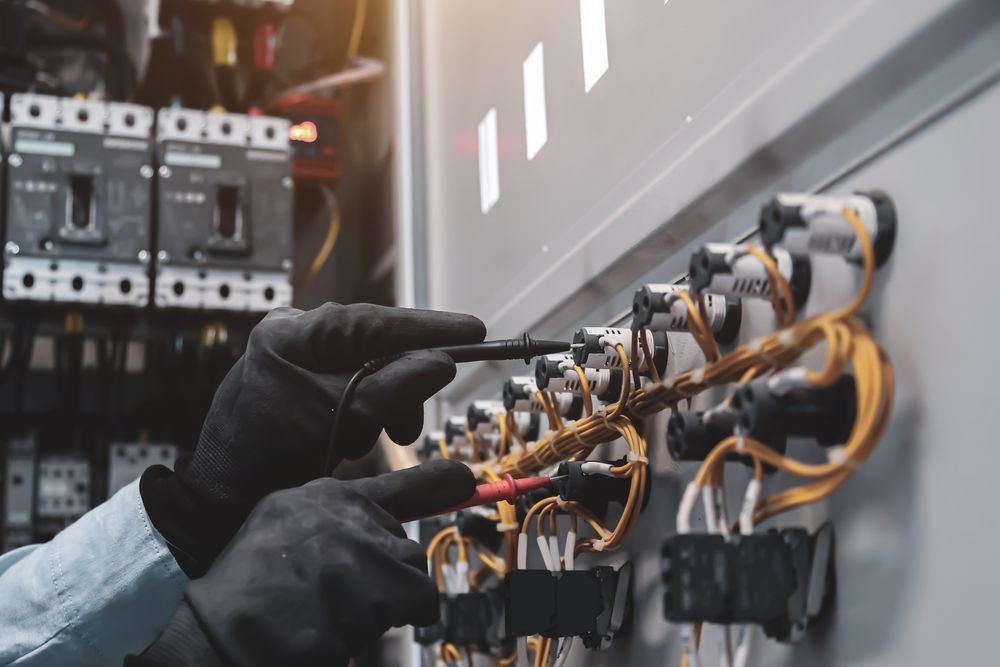 A person wearing protective gloves uses a multimeter probe to test electrical connections — AC/DC Electrical, Air Conditioning & Refrigeration In Zilzie, QLD