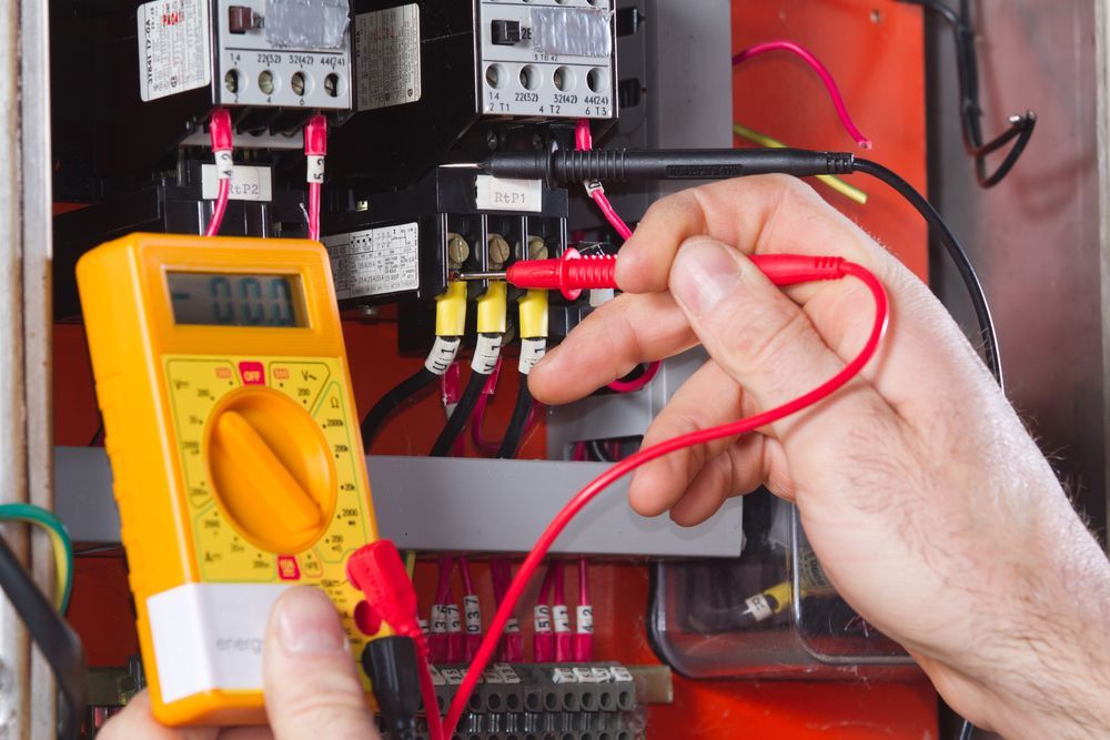 A hand uses a yellow multimeter to test voltage on an electrical panel with multiple wires and terminal connections. — AC/DC Electrical, Air Conditioning & Refrigeration In Zilzie, QLD