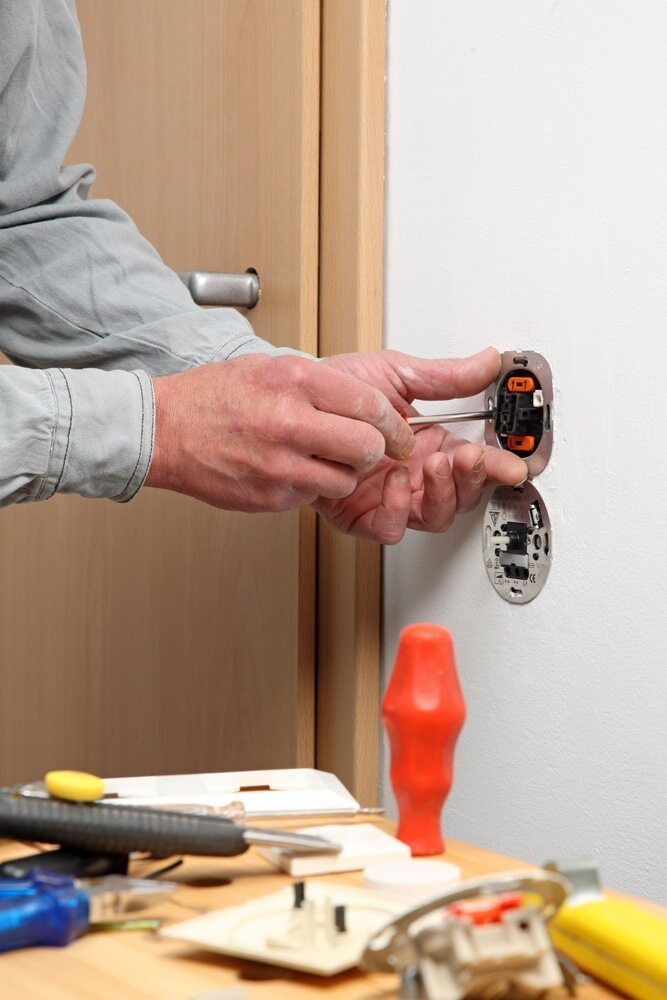 A Person Uses a Screwdriver to Install or Repair a Wall-Mounted Light Switch — AC/DC Electrical, Air Conditioning & Refrigeration In Plainlands, QLD