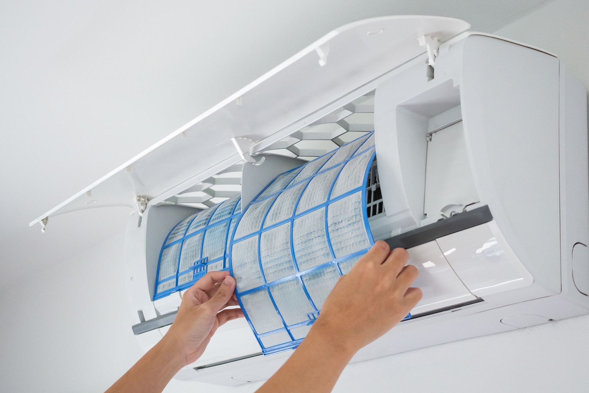 Hands Removing a Blue-Framed Air Conditioner Dust Filter — AC/DC Electrical, Air Conditioning & Refrigeration In Zilzie, QLD