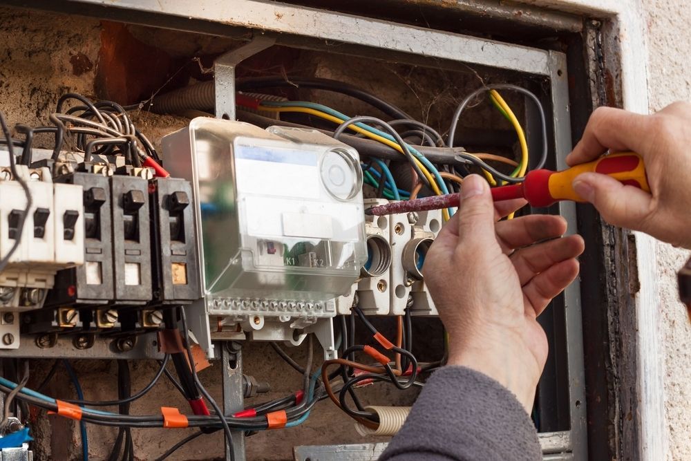 A Person Uses a Screwdriver to Work on The Electrical Wiring of An Open Meter Box — AC/DC Electrical, Air Conditioning & Refrigeration In Rockhampton, QLD