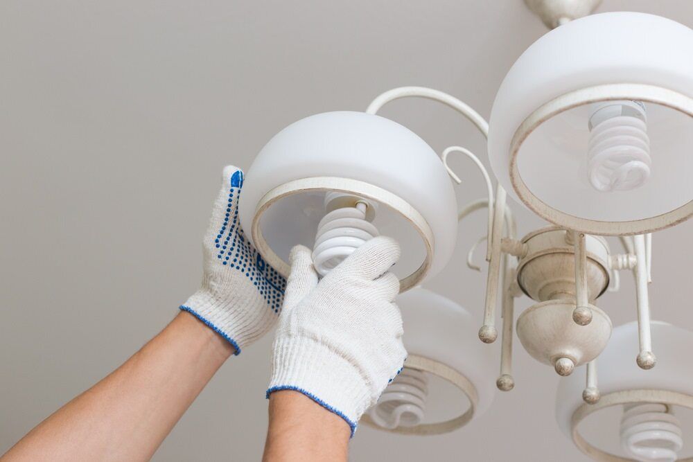 Hands in White Work Gloves Changing a Spiral Light Bulb in A White Chandelier — AC/DC Electrical, Air Conditioning & Refrigeration In Murphy's Creek, QLD