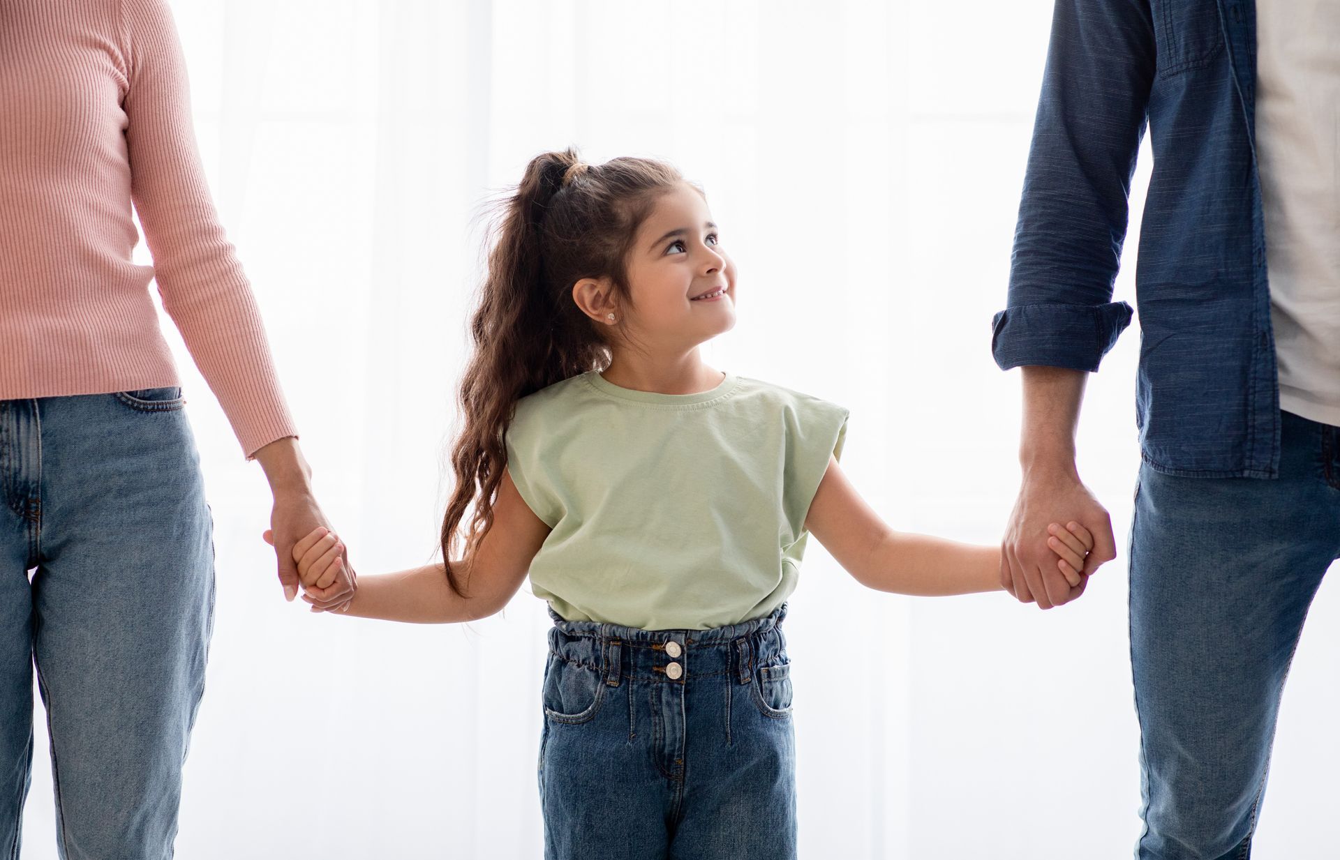 Child holding hands with two adults, smiling. All wearing jeans.
