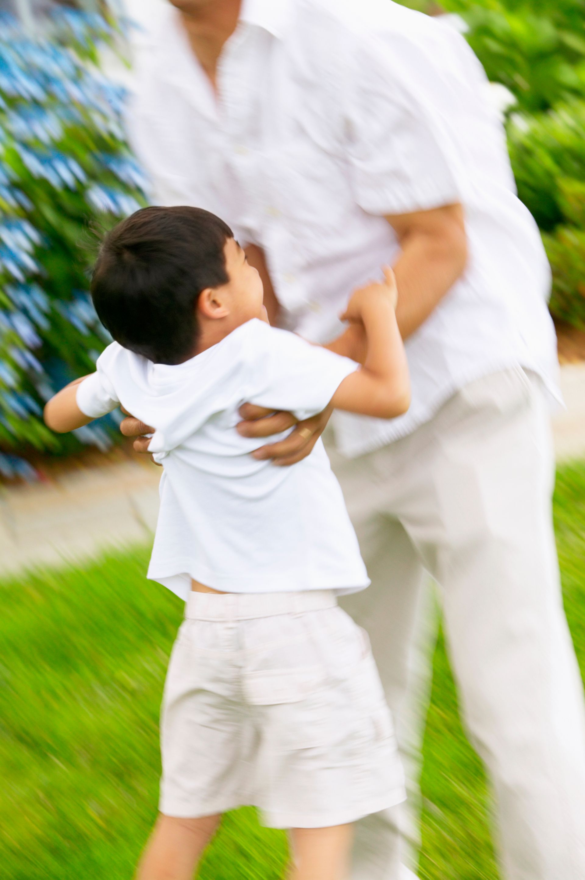 Man holding a child, both wearing white clothes, outdoors in a blurred setting.