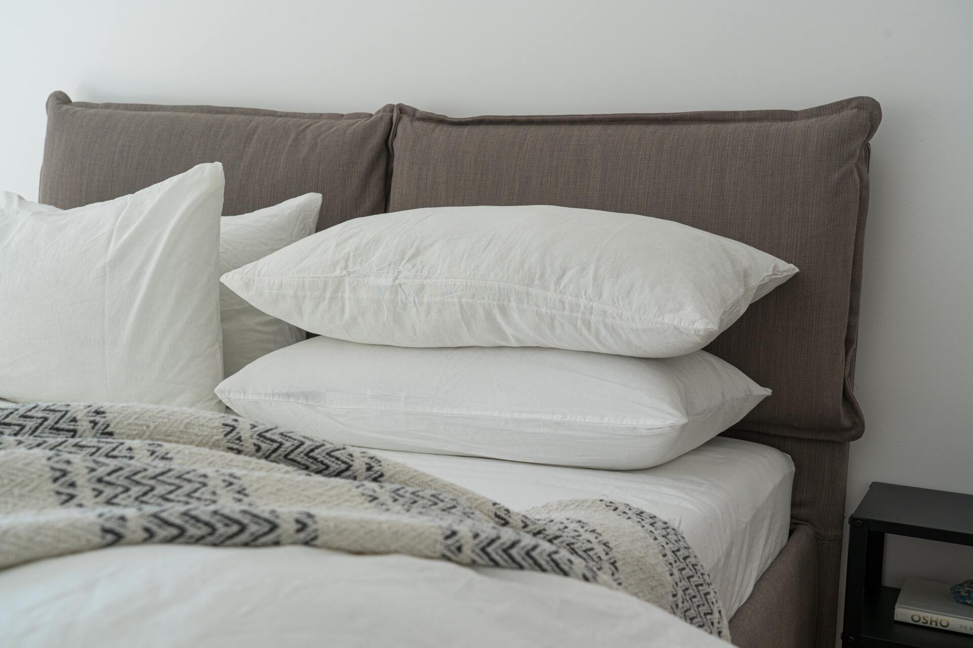 Neatly made bed with white and gray pillows and a patterned blanket in a bright bedroom