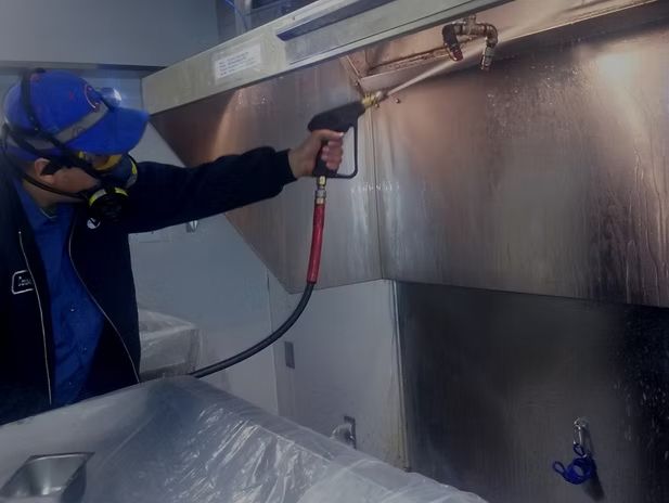 A worker is cleaning the stainless steel kitchen hood