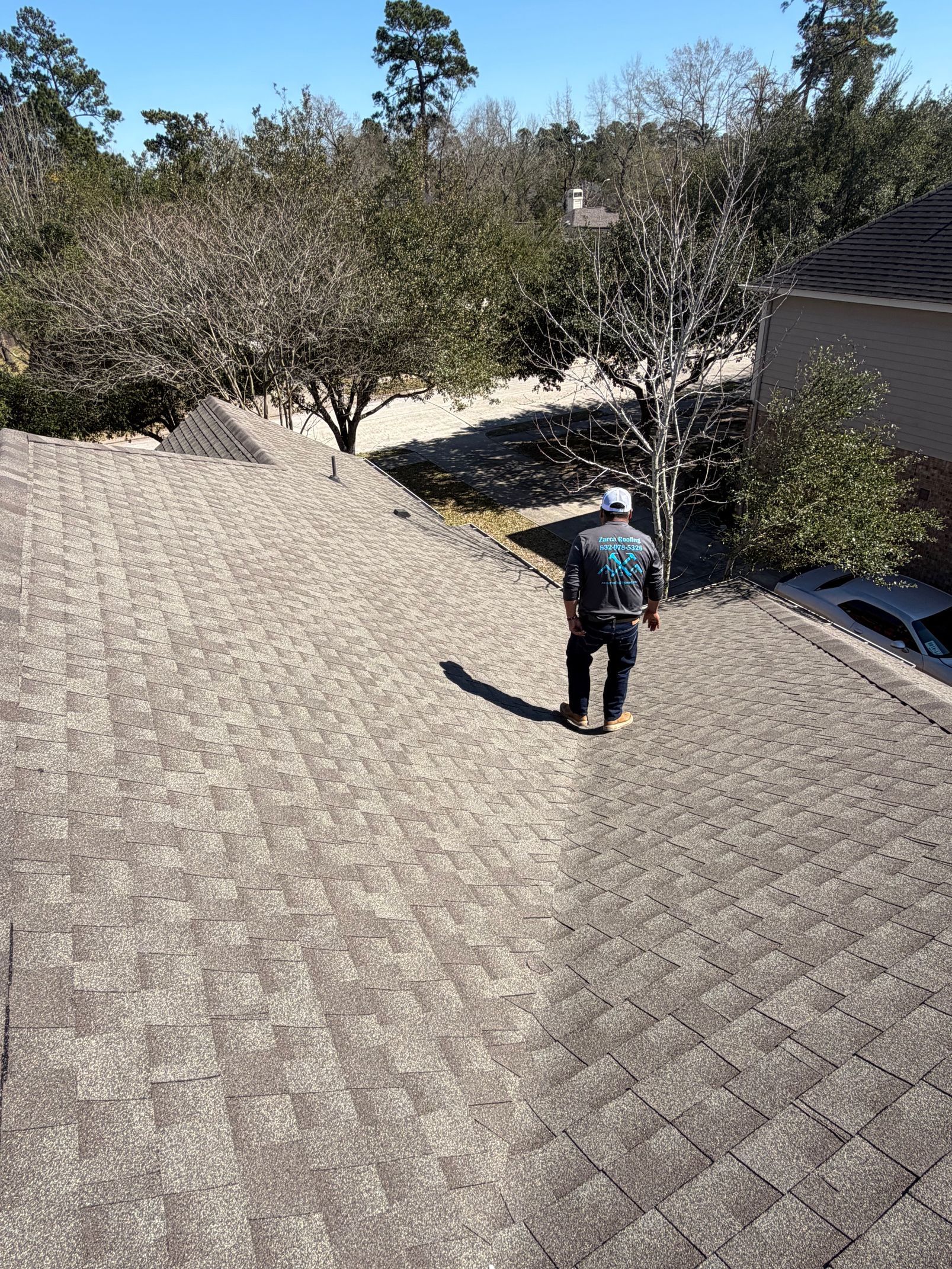 A person wearing a jacket and hat walks down a sloped, shingled residential roof on a sunny day.
