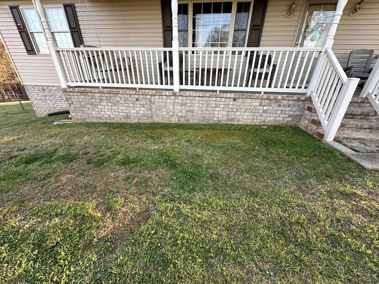 A lawn in front of a house with a porch and stairs.