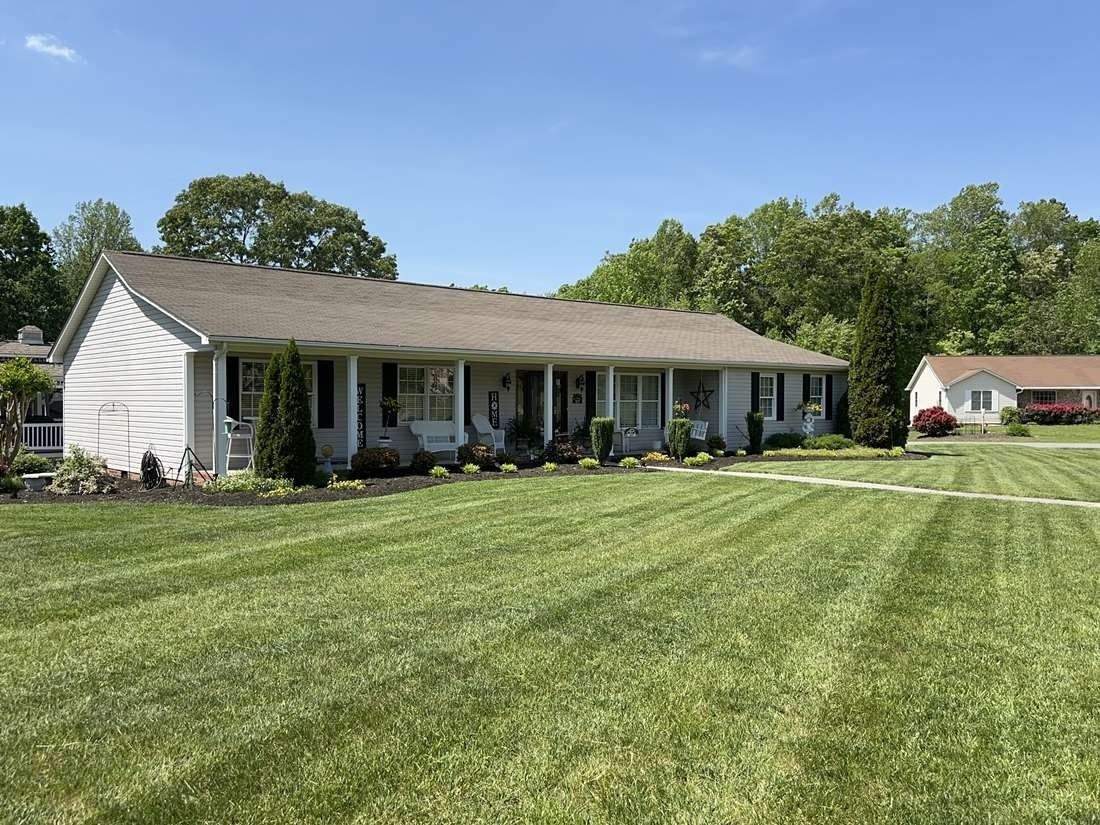A white house with a brown roof and a large lawn in front of it.