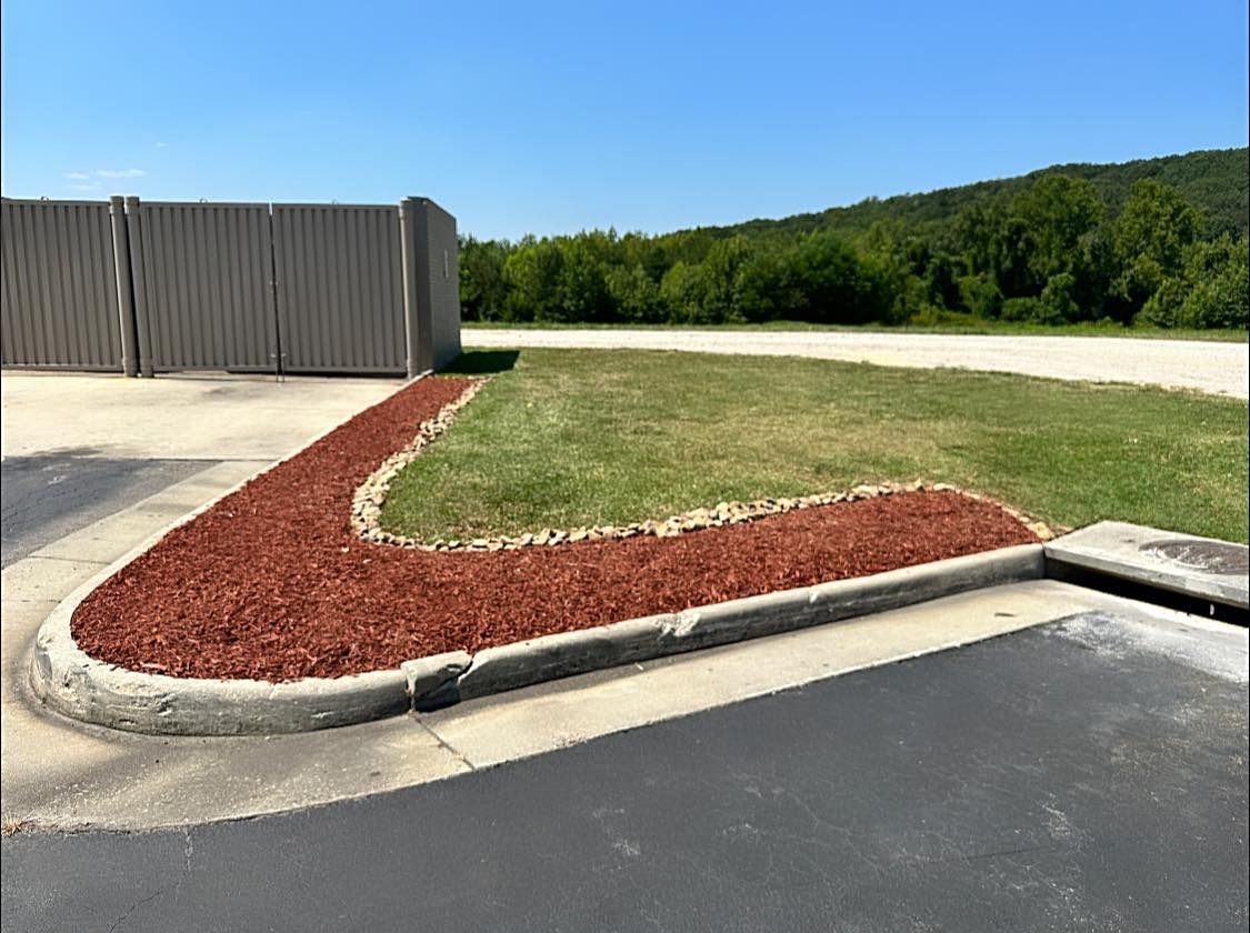 A sidewalk with red mulch and a fence in the background