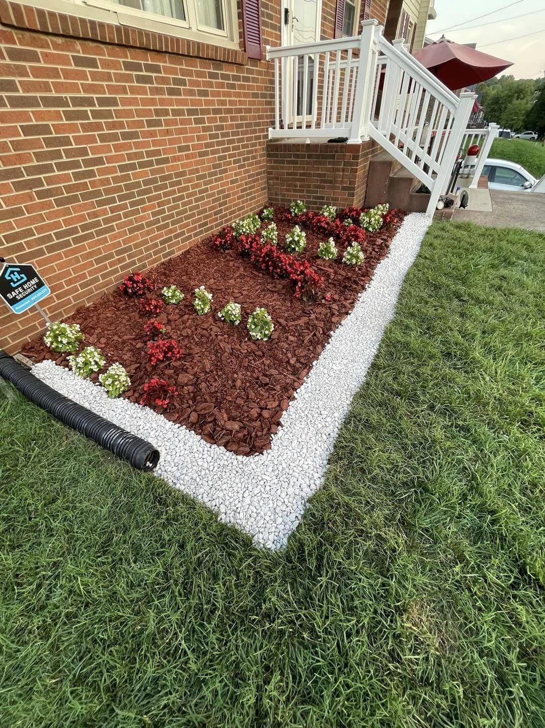 A garden with flowers and mulch in front of a brick house.
