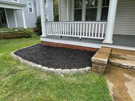 A house with a porch and black mulch in front of it.