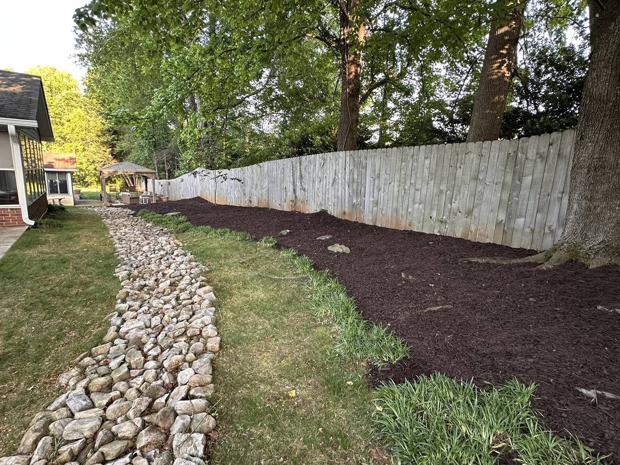 A stone wall surrounds a lush green yard with trees and mulch.