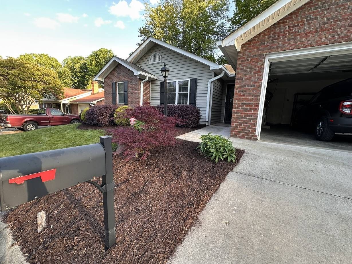 A mailbox is in front of a brick house with a car parked in the garage.