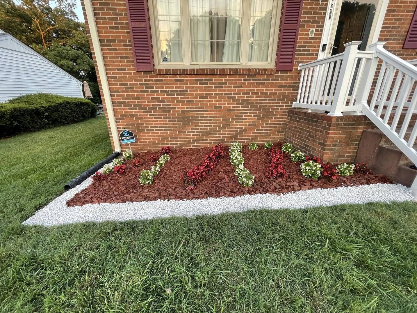 A brick house with a white railing and a garden in front of it.