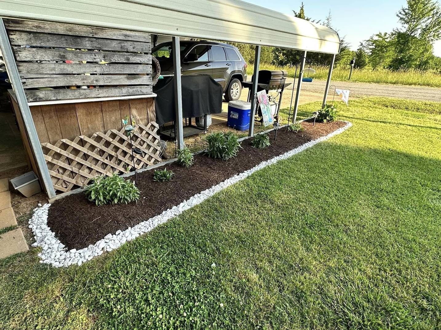 A car is parked under a carport in a yard.