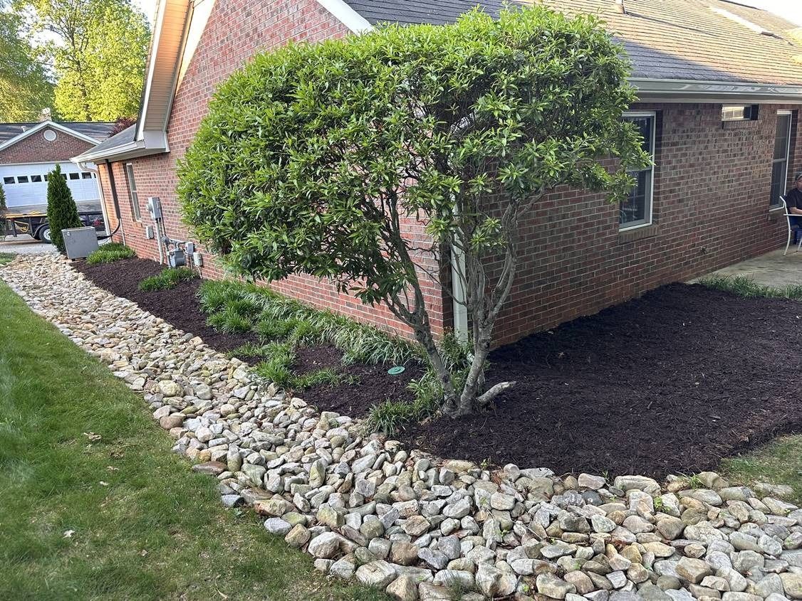 A brick house with a bush and rocks in front of it.