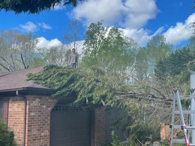 A man is standing on the roof of a house next to a ladder.