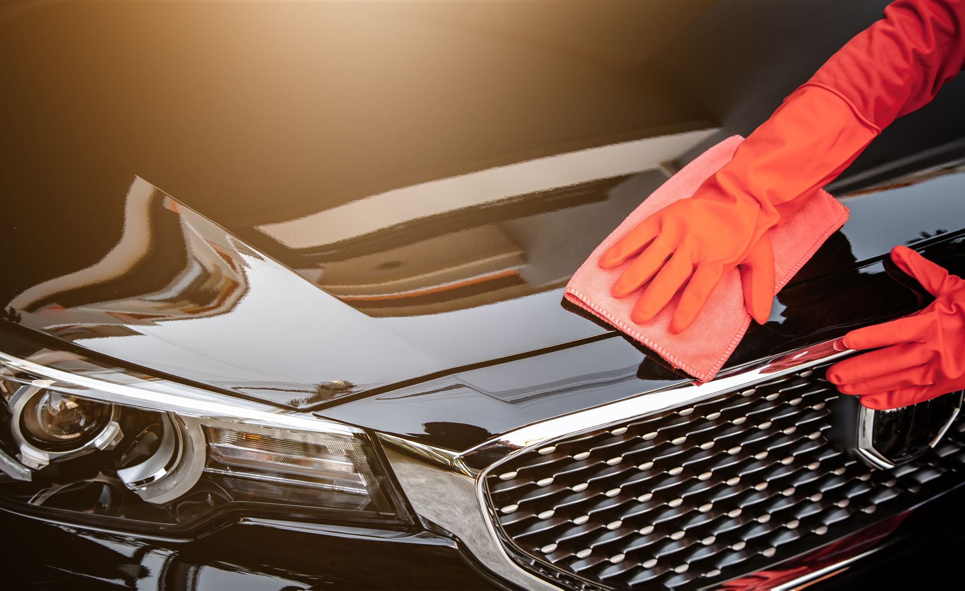 Gloved hands polishing the hood of a black car with a red cloth