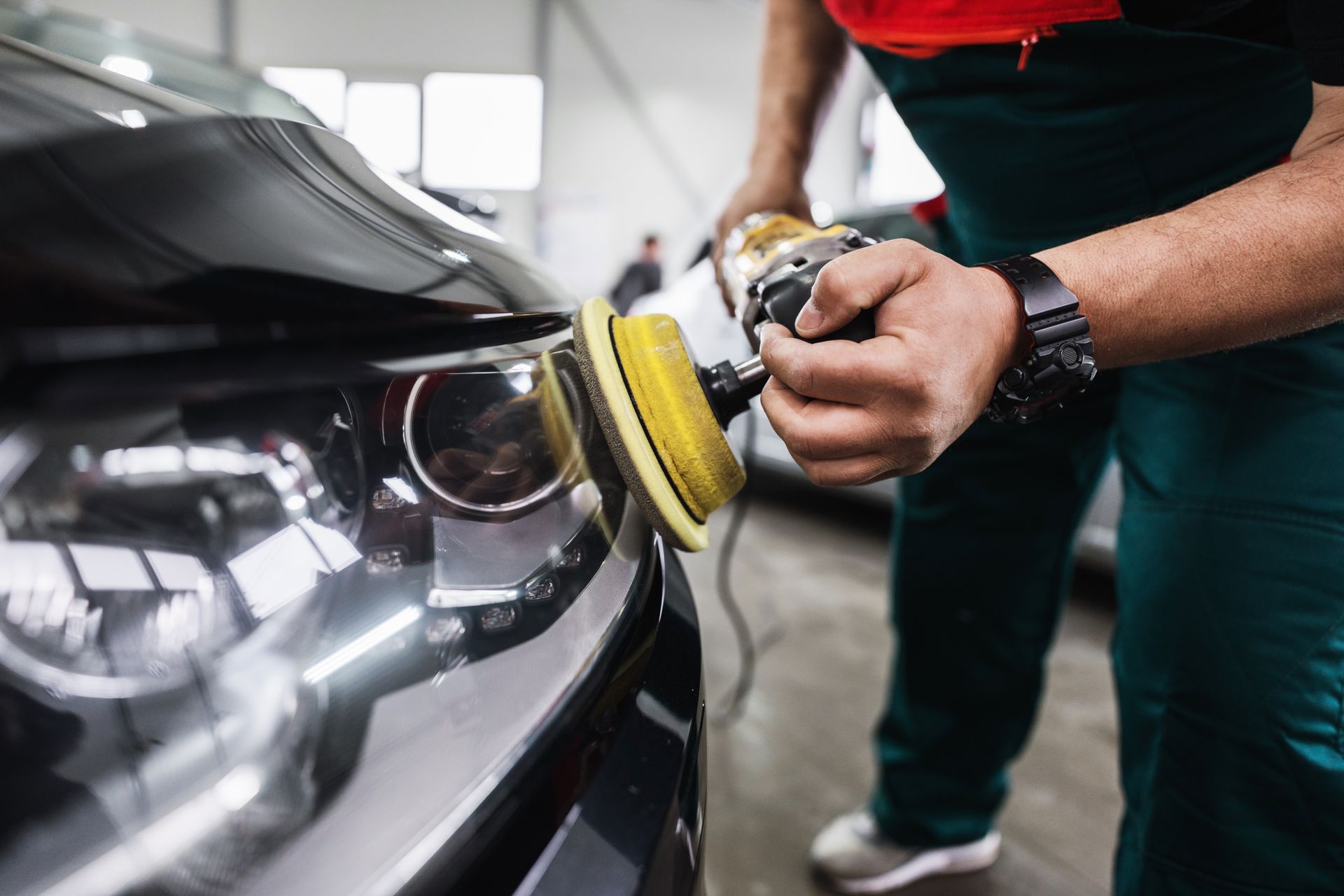 Person polishing a black car headlight with a buffer in a garage