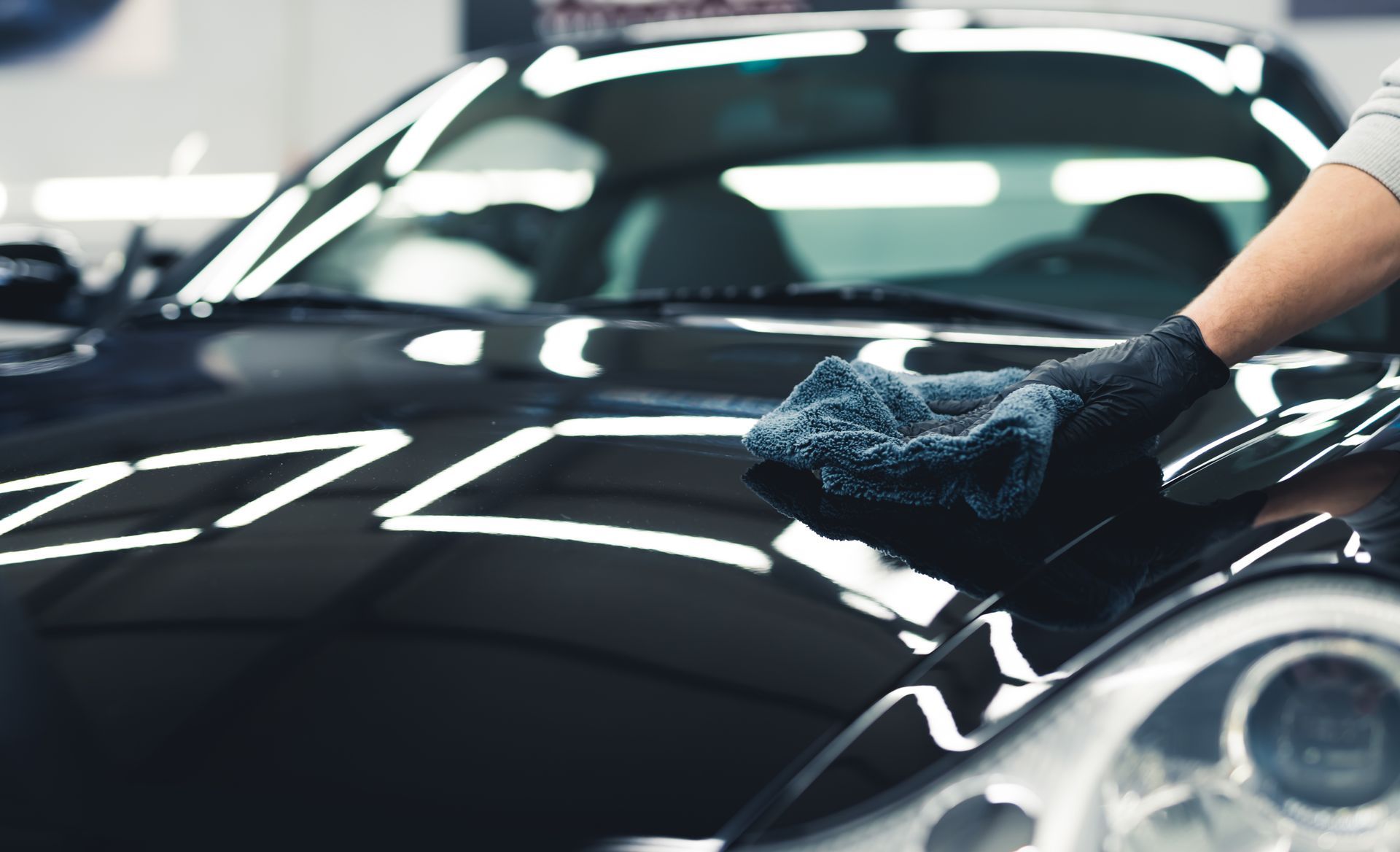 Person wiping a shiny black car hood with a cloth in a garage