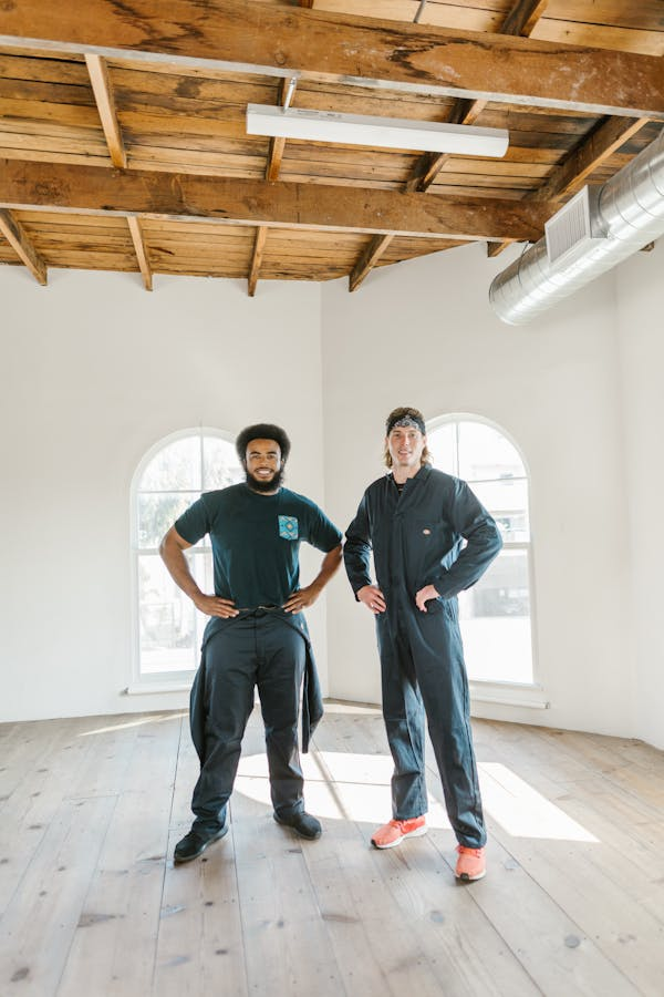 Two men in overalls are standing next to each other in an empty room.