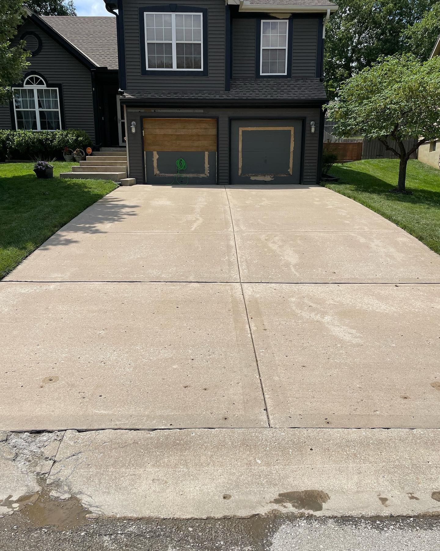 A concrete driveway leading to a house with two garage doors.