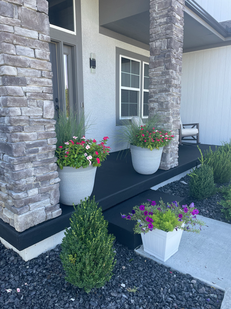 A front porch of a house with potted plants and flowers.