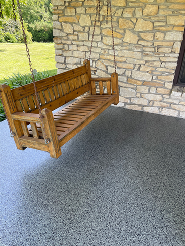 A wooden porch swing is hanging from a chain on a stone wall.
