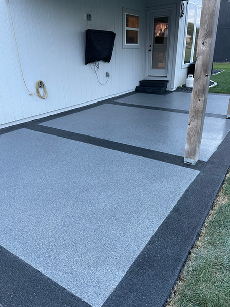 A concrete patio with a black border and a tv mounted on the wall.